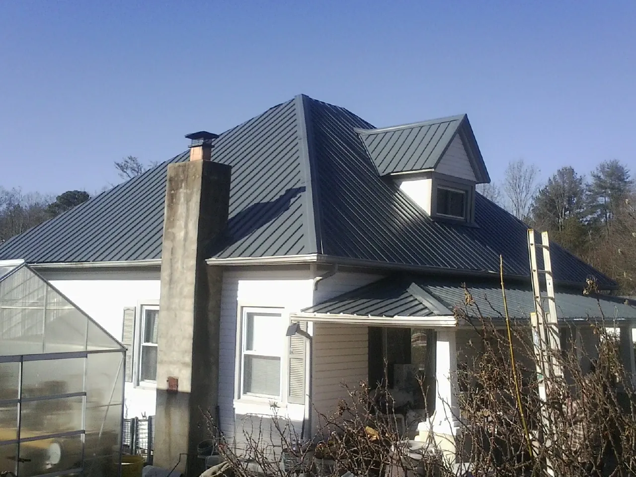 Dark blue standing seam metal roof on a white farmhouse with dormer — Slate & Tile Roof Repair by Roofing Brothers in Maple City