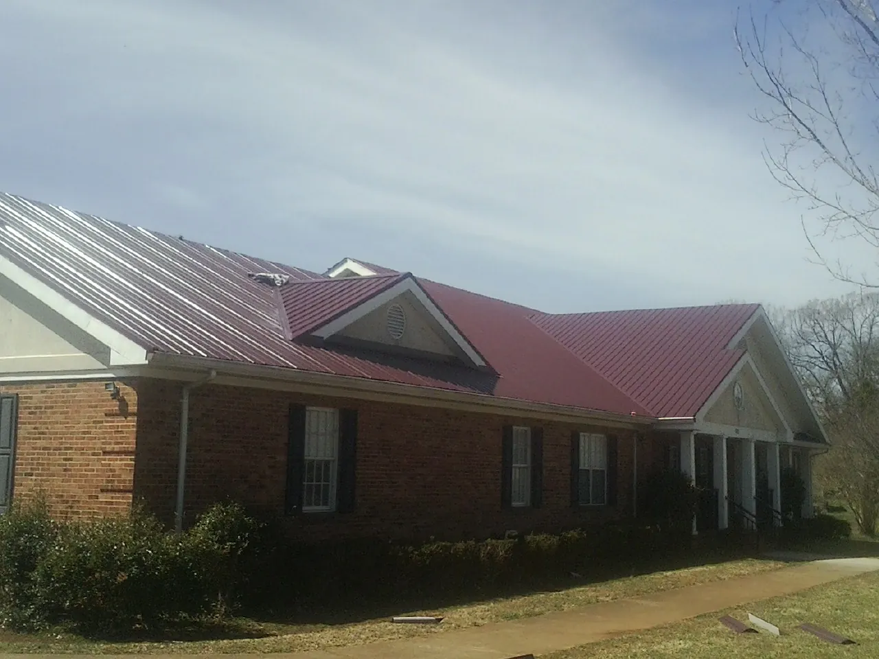 Red metal roof with gabled entries on a long brick building, from a Hail Damage Roof Repair job in Maple City