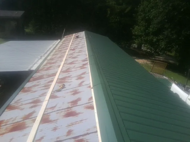 Old rusted panels beside newly installed green metal roofing — Wind Damage Roof Repair by Roofing Brothers in Maple City