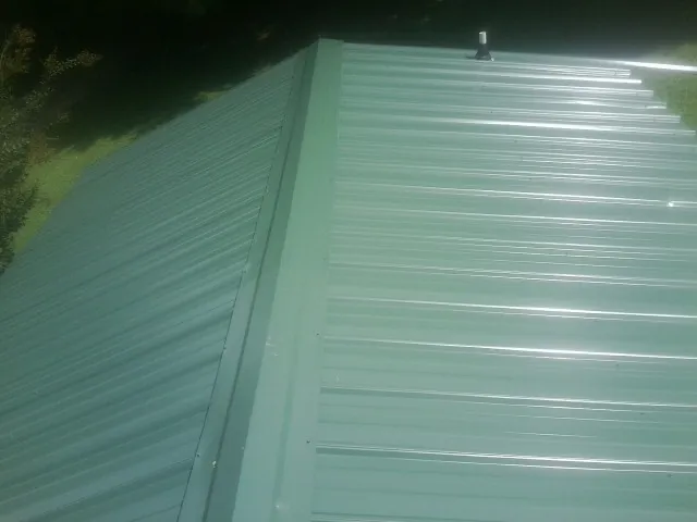 New green metal panels meeting at the ridge of a roof — Flat Roof Repair work by our crew in Maple City