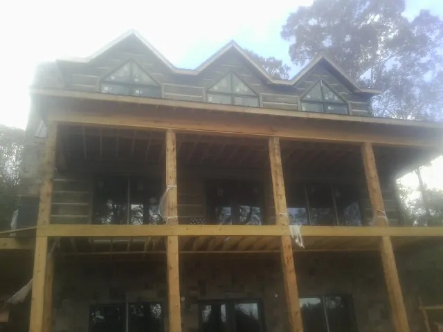 Dormers and porch framing on a large log home under construction — Roof Coating work by our crew in Maple City