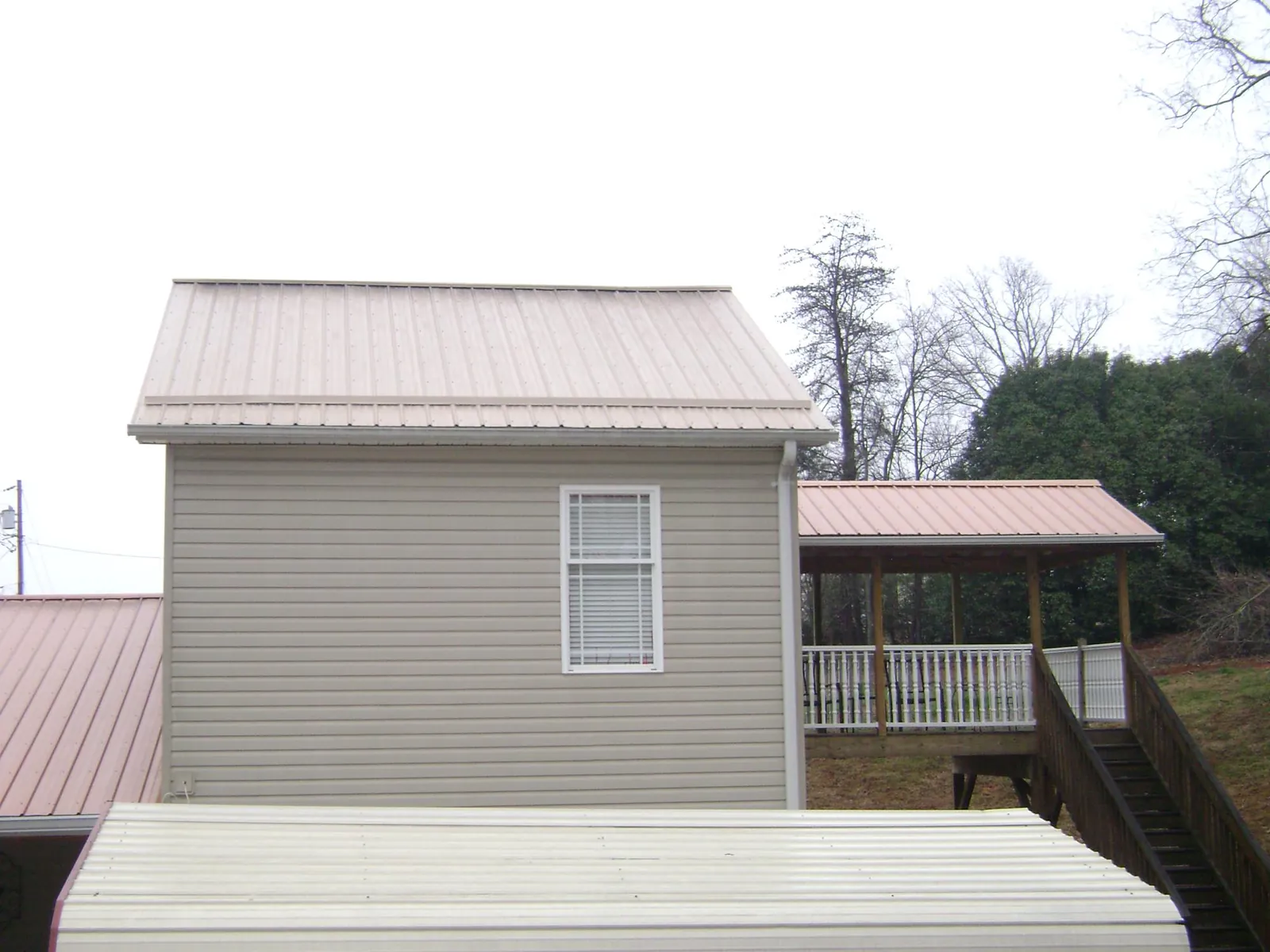 Tan metal roofs on a two story addition and attached porch, from a Roof Replacement job in Maple City
